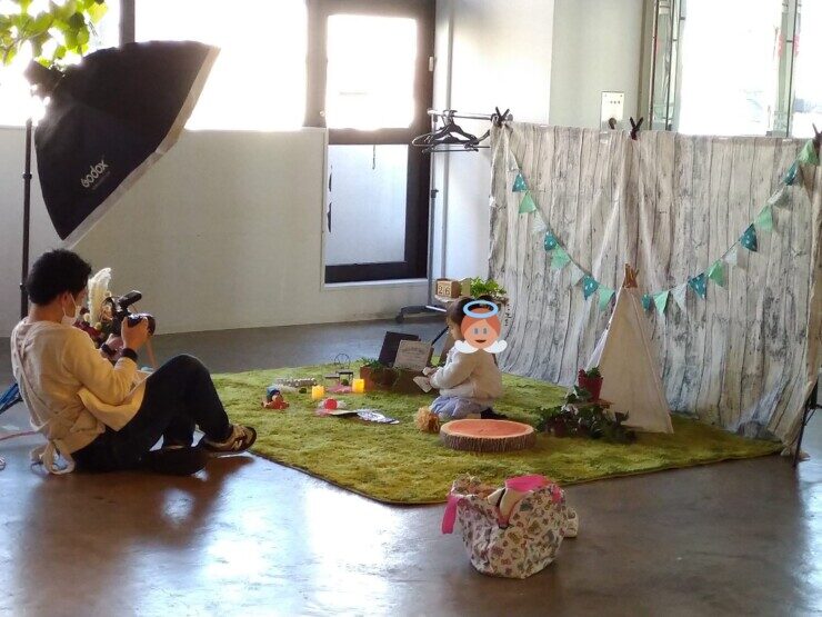 緑色のカーペットの上に座る子供の写真を撮るカメラマン